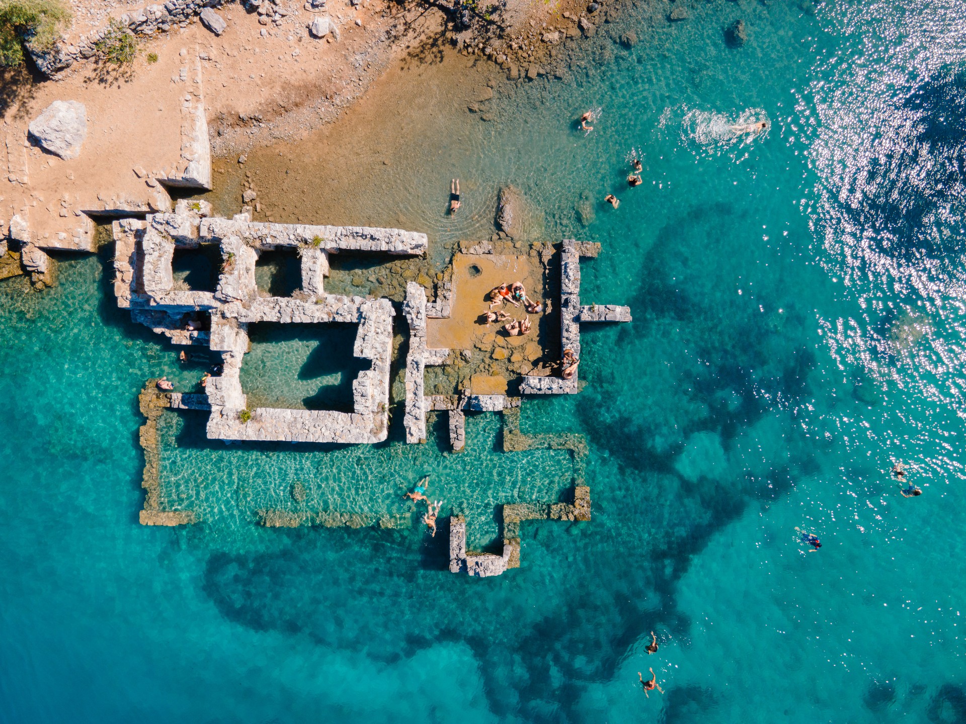 Aerial drone photo of swimmers enjoying the beautiful Kleopatra Hamami Cove, located between Göcek and Dalaman, Turkey, known for its crystal-clear waters and ancient ruins.