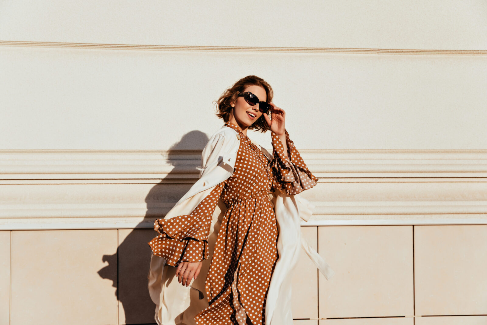 A pretty woman in a long brown dress enjoying a sunny day. Lovable white girl in retro attire walking down the street. (Adobe Stock Photo)