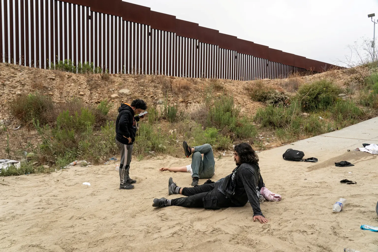 The two men lie on the ground in pain after falling from the border wall and injuring themselves, June 10, 2024. (Reuters Photo)