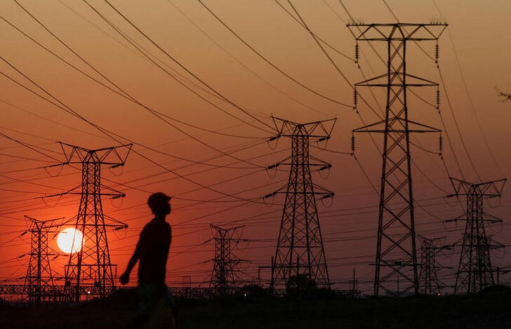 A local walks past electricity pylons during frequent power outages from South African utility Eskom, caused by its aging coal-fired plants, in Orlando, Soweto, South Africa, September 28, 2022. REUTERS/Siphiwe Sibeko/File Photo