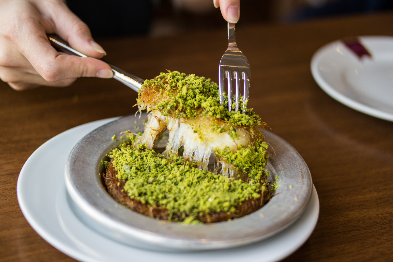 A warm, crispy dessert made with shredded phyllo dough, melted cheese, and sweet syrup, topped with pistachios. (Adobe Stock Photo)