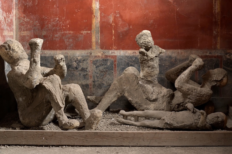 Mortuary casts of the victims of the House of the Golden Bracelet, Pompeii (Italy). In the background on the right, the supposed woman with a child. (Photo via Courtesy of MIC, Archaeological Park of Pompeii)