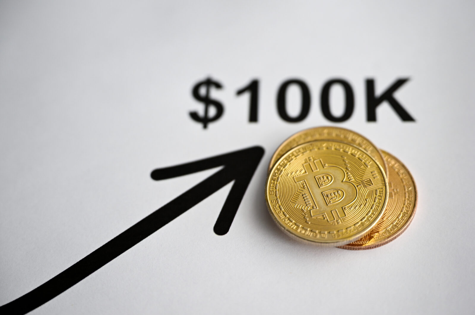 The photo illustration features two gold Bitcoin tokens placed on a white surface, alongside an upward arrow pointing toward '$100K in Ankara, Türkiye on Nov. 22, 2024. (AA Photo)