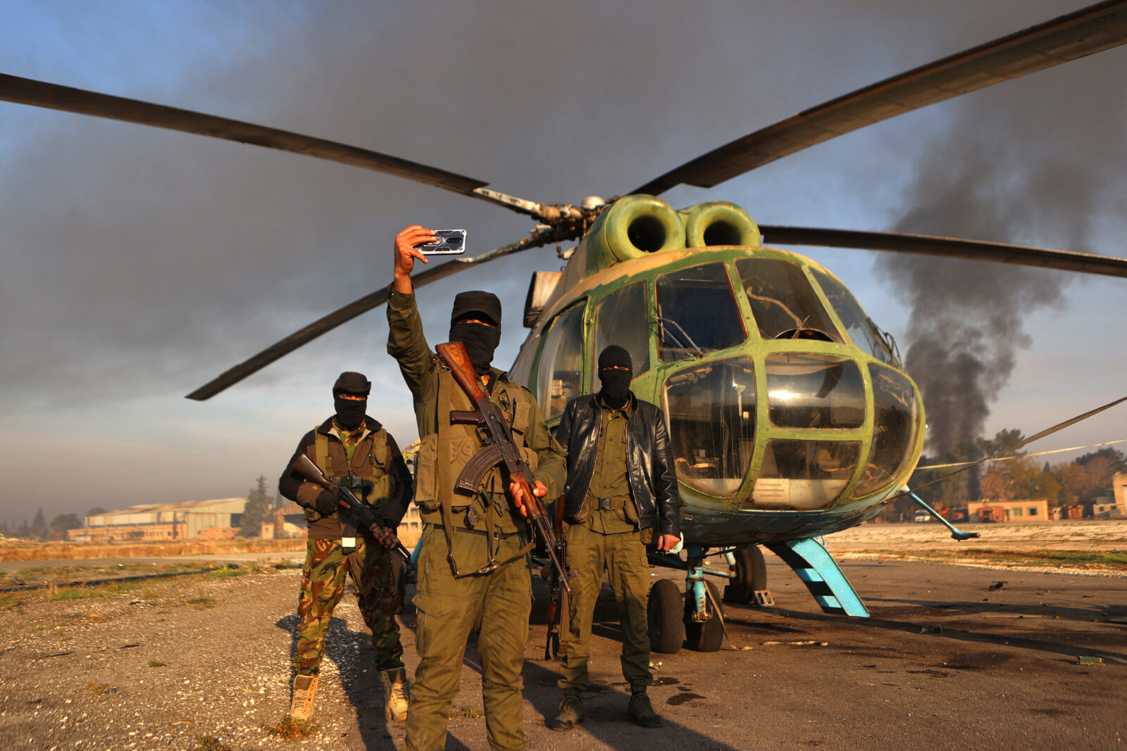Anti-regime fighters pose for a picture with an army helicopter on the tarmac at the Nayrab military airport in the northern Syrian city of Aleppo on December 2, 2024. - Islamist-led rebels on November 30, seized most of Aleppo, along with its airport and dozens of nearby towns, the war monitor Syrian Observatory for Human Rights said. (Photo by AAREF WATAD / AFP)People drive a motorcycle past abandoned Syrian army military equipment and vehicles, after anti-government fighters reached al-Safirah town southeast of Syria's Aleppo city on December 3, 2024. - On November 27, the Islamist Hayat Tahrir al-Sham (HTS) alliance led a major offensive snatching Syria's second city Aleppo and dozens of towns and villages from government control, after years of regime gains in successive Russian-backed military campaigns. (Photo by Aref TAMMAWI / AFP)Syrian army jets sit on the tarmac the Nayrab military airport in the northern Syrian city of Aleppo on December 2, 2024. - Islamist-led rebels on November 30, seized most of Aleppo, along with its airport and dozens of nearby towns, the war monitor Syrian Observatory for Human Rights said. (Photo by AAREF WATAD / AFP)Fighters from Hayat Tahrir al-Sham (HTS) gather at a position in the eastern outskirts of the town of Atarib, in Syria's northern province of Aleppo on November 27, 2024, during clashes with the Syrian army. - At least 57 people were killed in clashes sparked by a surprise jihadist attack on the Syrian army, a war monitor said. (Photo by Abdulaziz KETAZ / AFP)