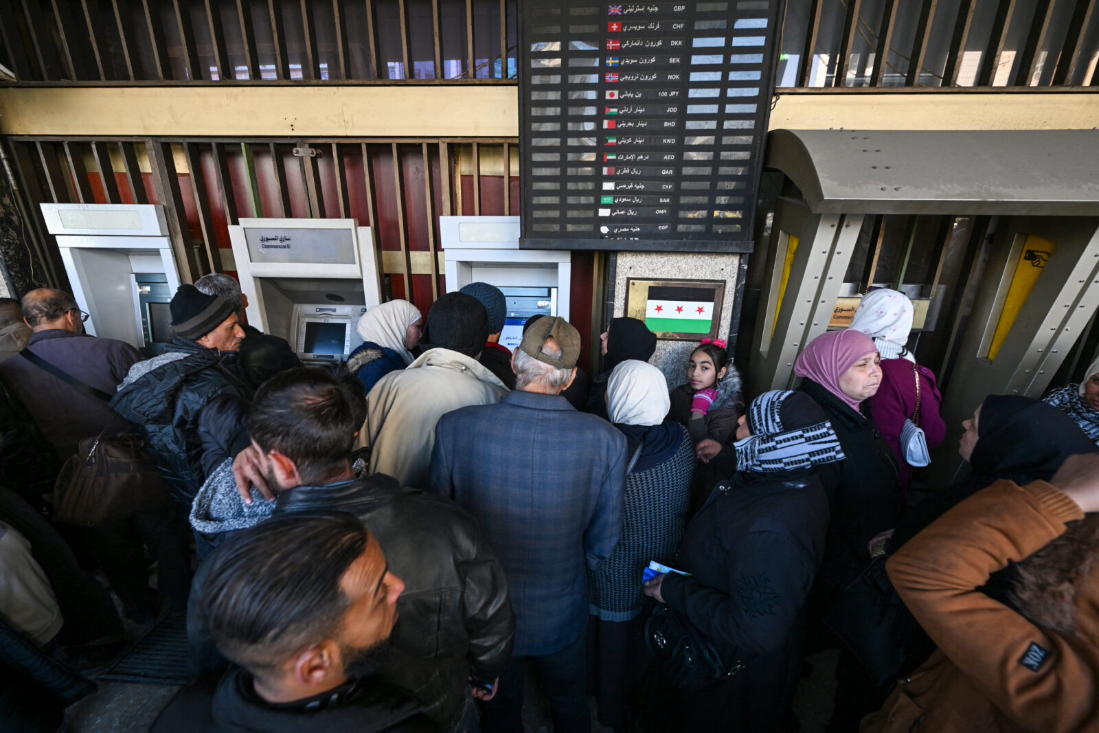 People queue to use ATM machines outside a bank in Damascus on December 16, 2024. - Governments worldwide are stepping up efforts to engage with Syria's new interim rulers, just over a week after Islamist-led rebels ousted president Bashar al-Assad, ending decades of brutal rule and civil war. (Photo by LOUAI BESHARA / AFP)A customer makes a transaction in US dollars at a commercial bank affiliated with the central bank in Damascus on December 16, 2024. - Governments worldwide are stepping up efforts to engage with Syria's new interim rulers, just over a week after Islamist-led rebels ousted president Bashar al-Assad, ending decades of brutal rule and civil war. (Photo by Louai Beshara / AFP) / The erroneous CAPTION appearing in the metadata of this photo by Louai Beshara has been modified in AFP systems. Please immediately remove the erroneous mention[s] from all your online services and delete it (them) from your servers. If you have been authorized by AFP to distribute it (them) to third parties, please ensure that the same actions are carried out by them. Failure to promptly comply with these instructions will entail liability on your part for any continued or post notification usage. Therefore we thank you very much for all your attention and prompt action. We are sorry for the inconvenience this notification may cause and remain at your disposal for any further information you may require.A teller counts US dollars at a commercial bank affiliated with the central bank in Damascus on December 16, 2024. - Governments worldwide are stepping up efforts to engage with Syria's new interim rulers, just over a week after Islamist-led rebels ousted president Bashar al-Assad, ending decades of brutal rule and civil war. (Photo by Louai Beshara / AFP) / The erroneous CAPTION appearing in the metadata of this photo by Louai Beshara has been modified in AFP systems. Please immediately remove the erroneous mention[s] from all your online services and delete it (them) from your servers. If you have been authorized by AFP to distribute it (them) to third parties, please ensure that the same actions are carried out by them. Failure to promptly comply with these instructions will entail liability on your part for any continued or post notification usage. Therefore we thank you very much for all your attention and prompt action. We are sorry for the inconvenience this notification may cause and remain at your disposal for any further information you may require.An employee counts Syrian pounds at a commercial bank affiliated with the central bank in Damascus on December 16, 2024. - Governments worldwide are stepping up efforts to engage with Syria's new interim rulers, just over a week after Islamist-led rebels ousted president Bashar al-Assad, ending decades of brutal rule and civil war. (Photo by Louai Beshara / AFP) / The erroneous CAPTION appearing in the metadata of this photo by Louai Beshara has been modified in AFP systems. Please immediately remove the erroneous mention[s] from all your online services and delete it (them) from your servers. If you have been authorized by AFP to distribute it (them) to third parties, please ensure that the same actions are carried out by them. Failure to promptly comply with these instructions will entail liability on your part for any continued or post notification usage. Therefore we thank you very much for all your attention and prompt action. We are sorry for the inconvenience this notification may cause and remain at your disposal for any further information you may require.