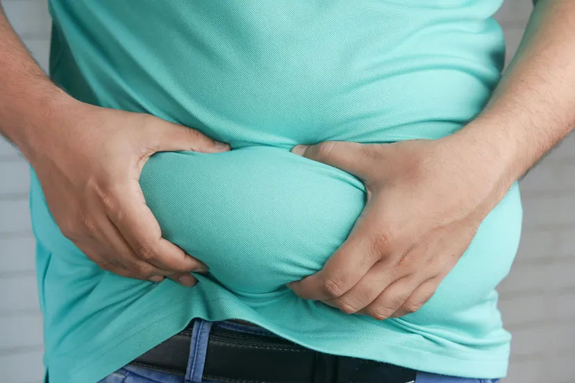 Someone holding their belly because of excess weight. (Photo via Towfiqu barbhuiya on Unsplash)