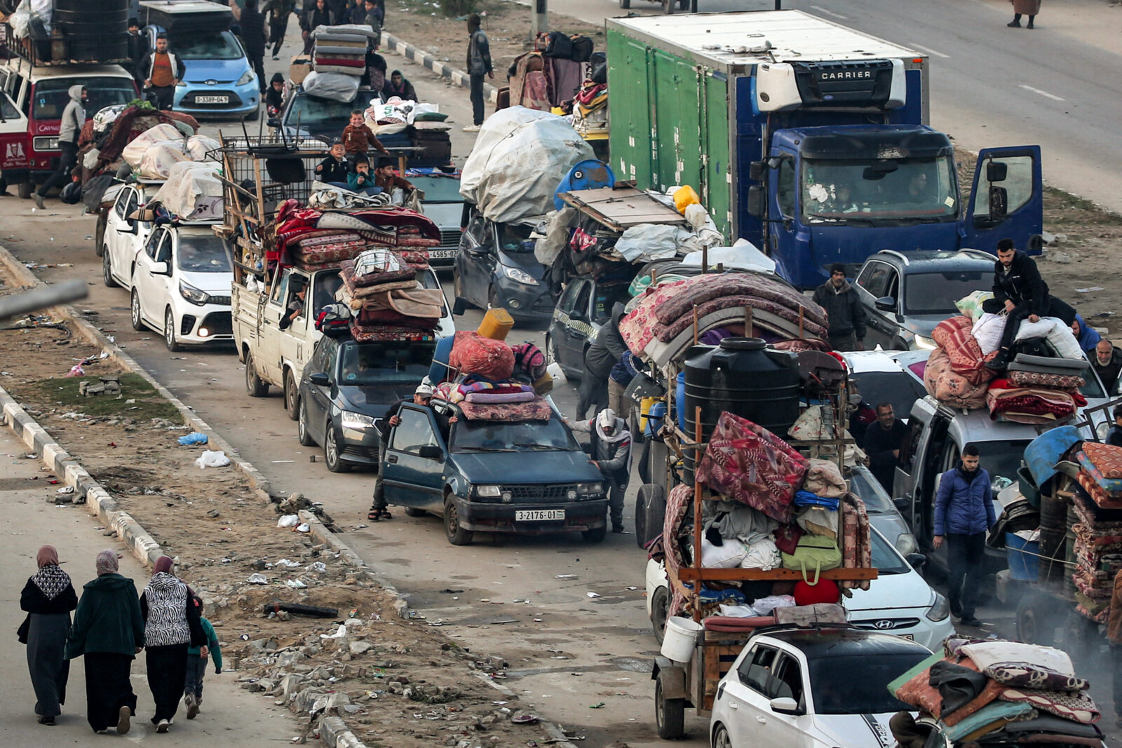 Three women walk past a queue of vehicles waiting along the Salah al-Din road in Nuseirat near the Netzarim corridor to cross to the northern part of the Gaza Strip on Jan. 27, 2025. (AFP Photo)