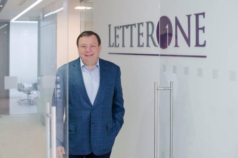 Russian billionaire Mikhail Fridman stands near a glass door with the 