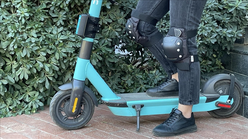 A person stands on an electric scooter wearing protective gear. (AA Photo)