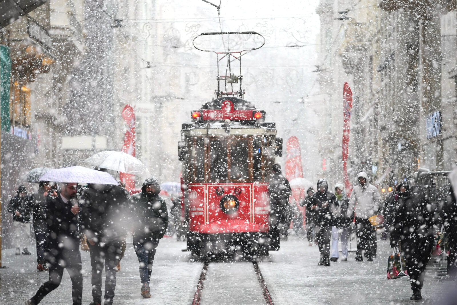 People walk with umbrellas on Istiklal Street as the nostalgic tram operates during the snowfall in Taksim, Beyoglu district, Istanbul, Türkiye, Feb. 19, 2025. (AA Photo)
