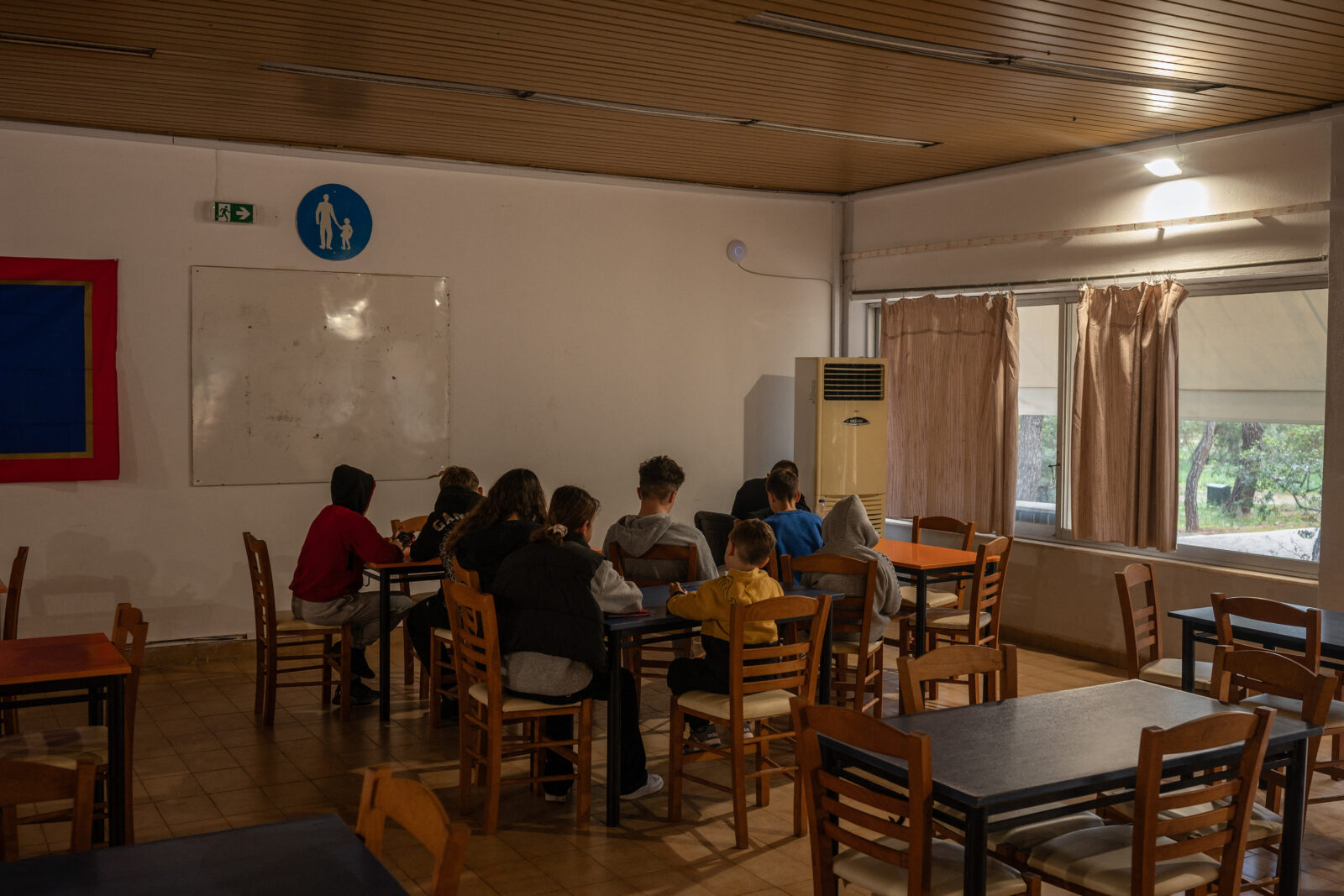 A small group of teenagers and children check their tablets and smartphones while sitting in the cafeteria of a summer camp run by the city of Athens, in Agios Andreas, Feb. 18, 2025. (AFP Photo)