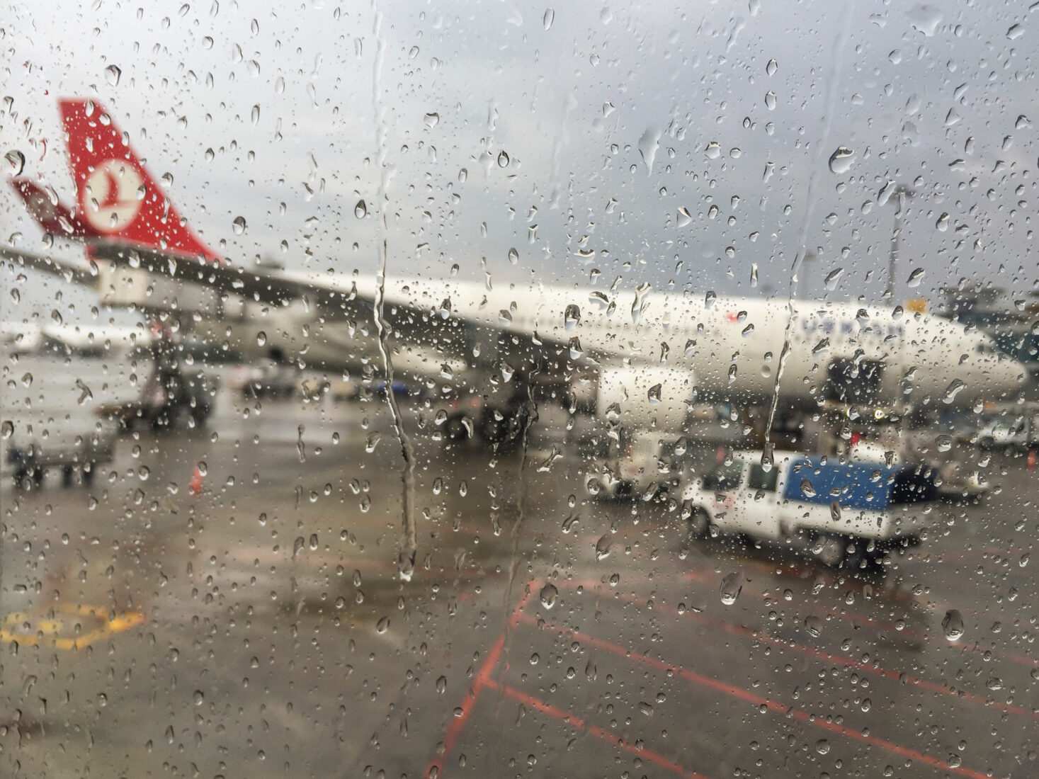 The file photo shows a blurred view of a Turkish Airlines aircraft parked at the gate through an airport window covered with raindrops. (Adobe Stock Photo)