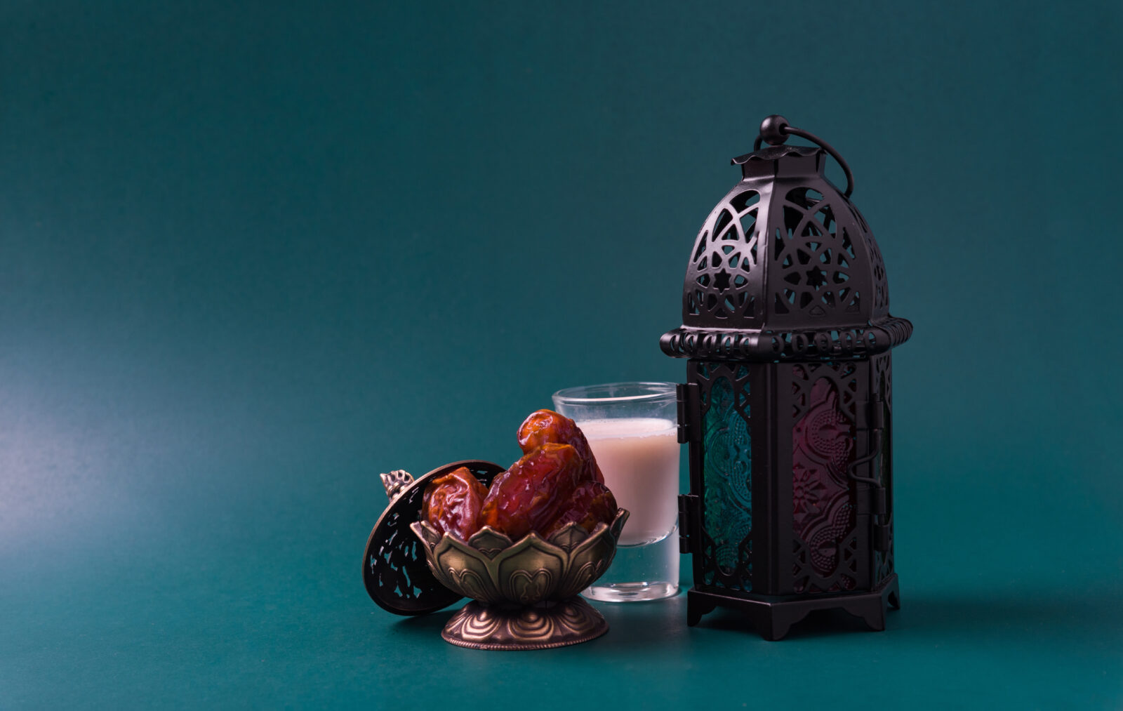 A decorative lantern dates in an ornate bowl, and a glass of milk on a dark green background, symbolize iftar during Ramadan, Türkiye. (Adobe Stock Photo)