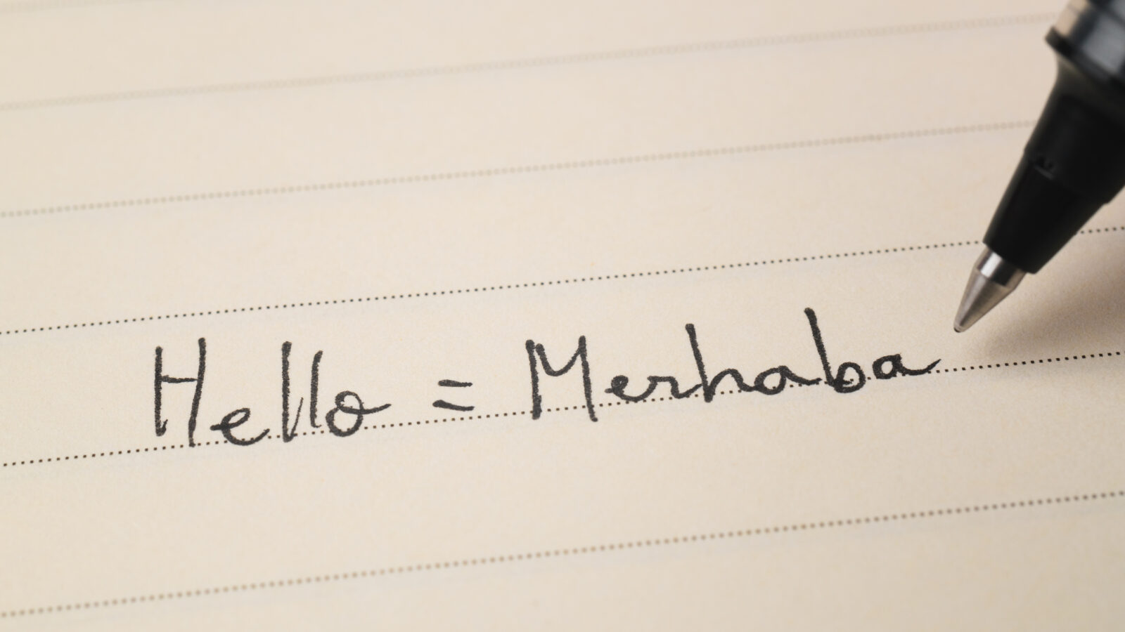A beginner Turkish language learner writing 'Hello=Merhaba' for homework, captured in a close-up shot of a notebook. (Adobe Stock Photo)