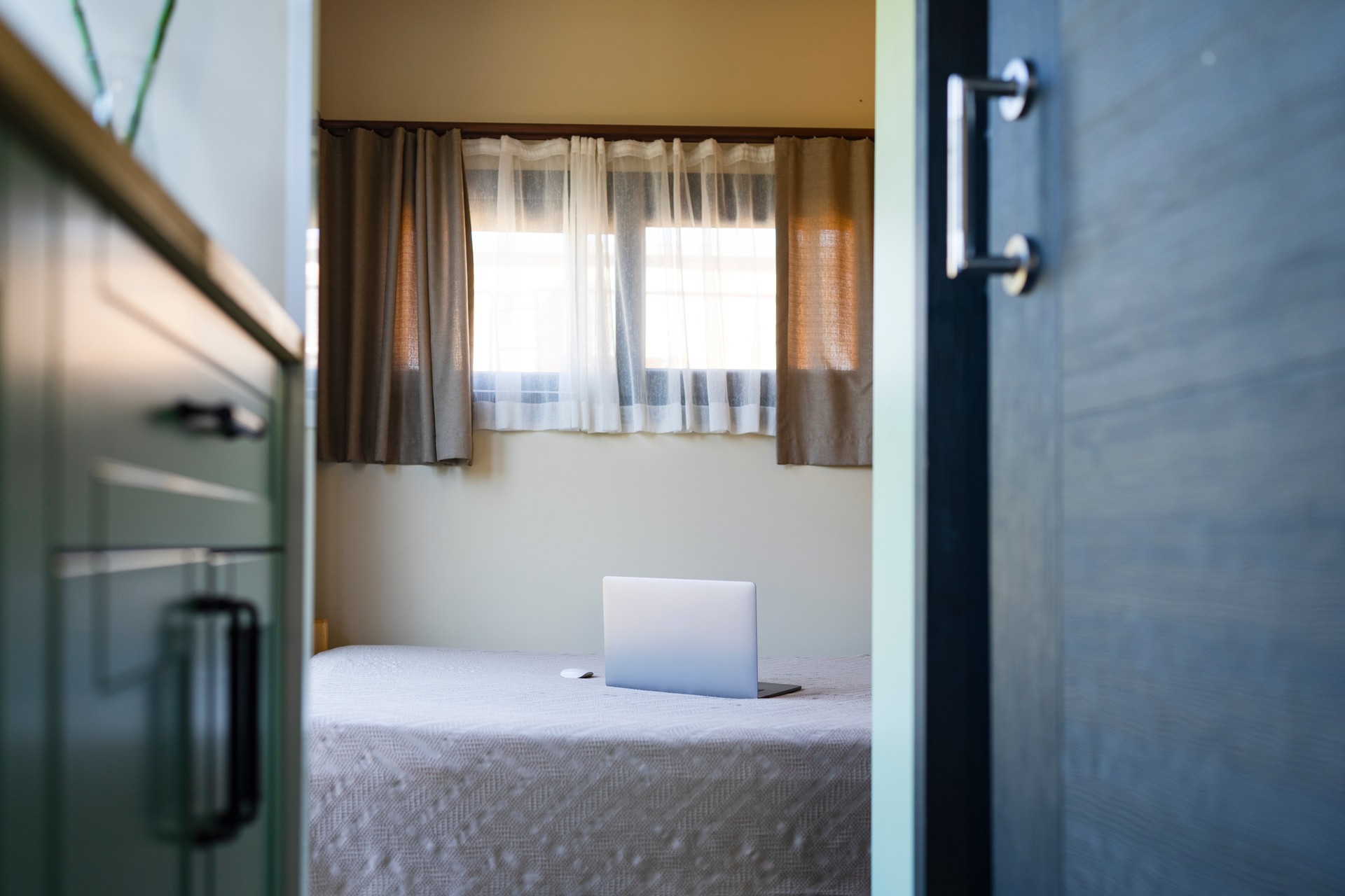 A hotel room with an open laptop sitting on a neatly made bed. (Adobe Stock Photo)