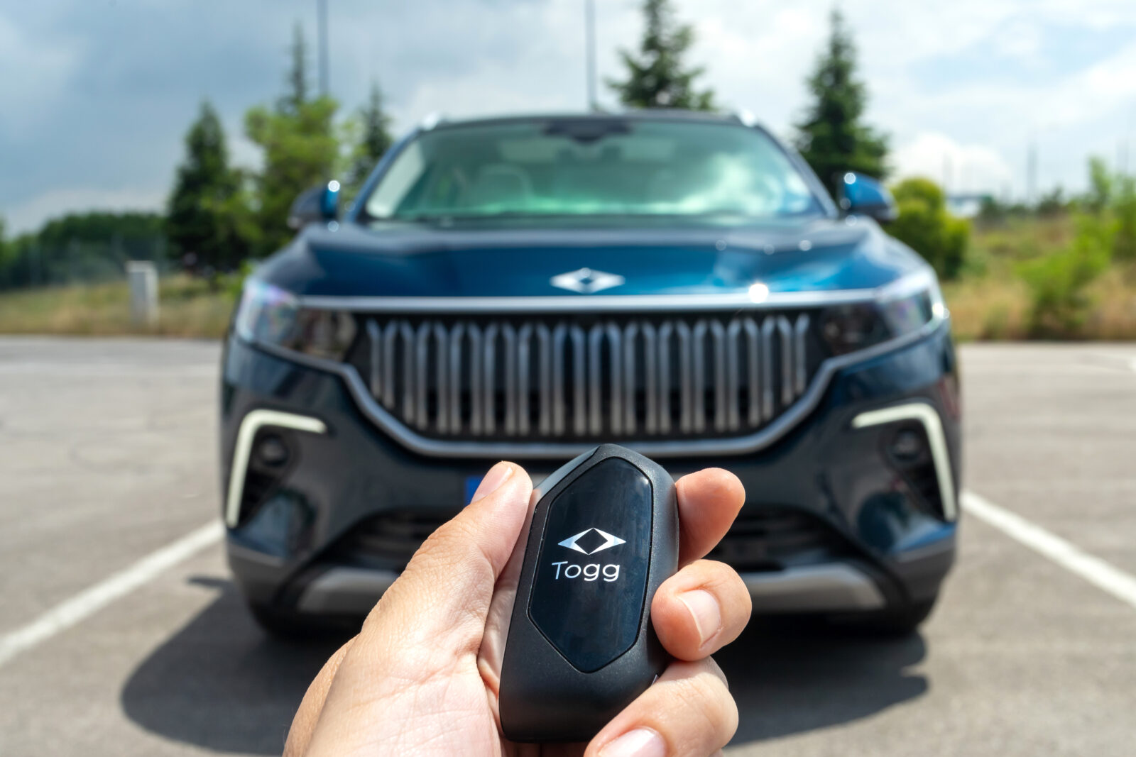 The file photo shows a close-up of a person holding a Togg-branded car key fob in front of a Togg electric vehicle (EV) parked outdoors. (Adobe Stock Photo)