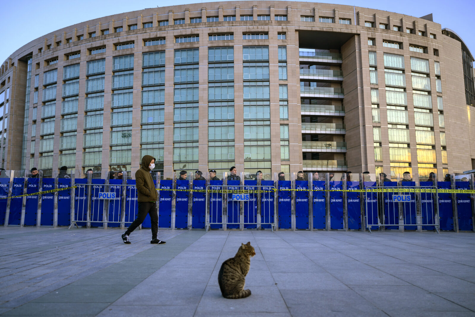 A cat sits as a person walks by police forces cordoning off the area outside the Caglayan courthouse where Istanbul mayor Ekrem Imamoglu is due to appear before prosecutors following his arrest in connection with a corruption probe, in Istanbul, on March 22, 2025. (Photo by Yasin AKGUL / AFP)