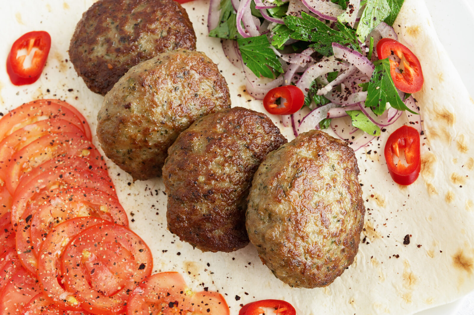 Crisp and golden Turkish meatballs (Kuru Kofte) served with fresh tomatoes, onions, and sumac salad, ideal for a comforting main course to your iftar meal. (Adobe Stock Photo)