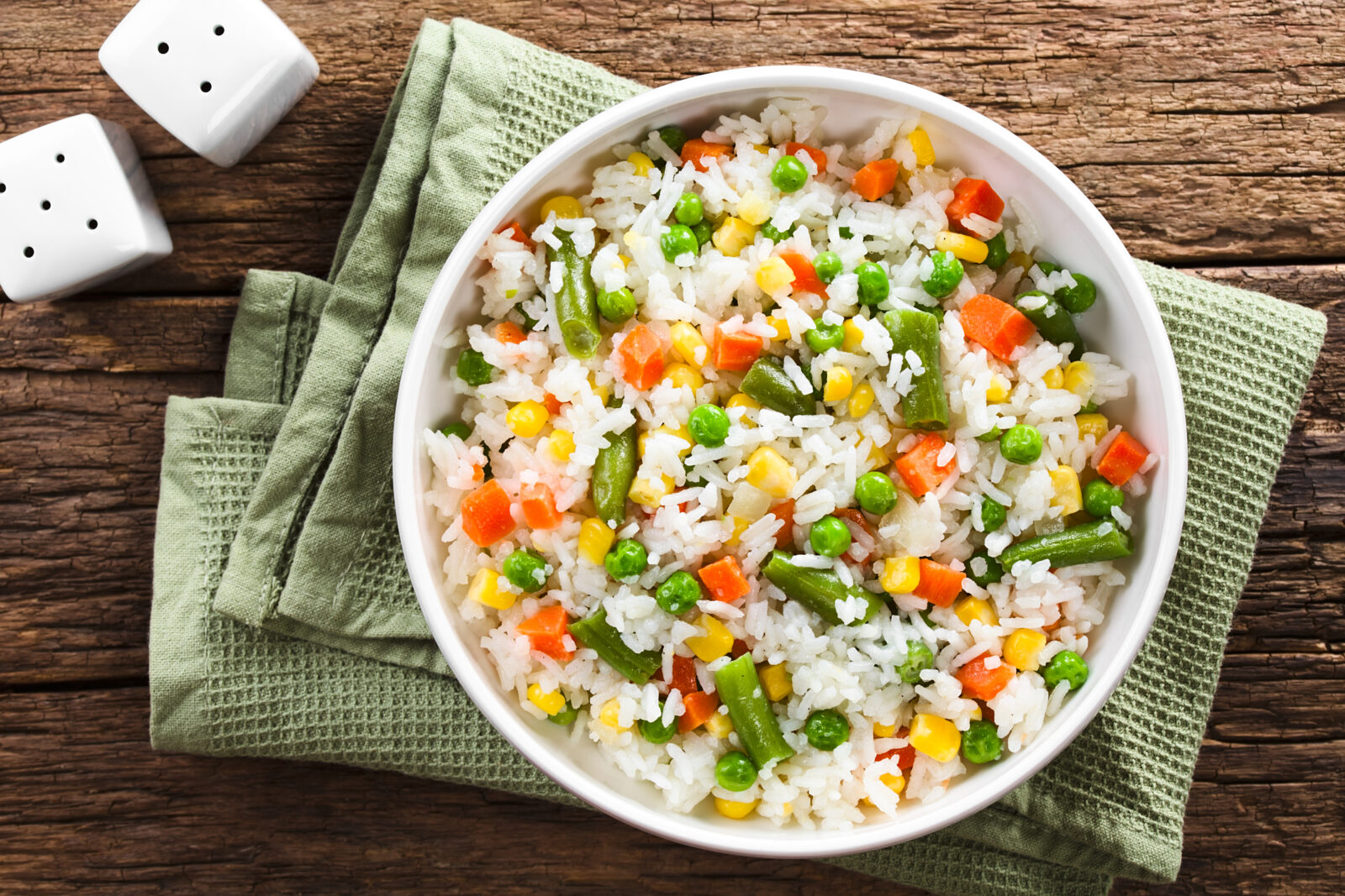 A bowl of Turkish-style garnished rice pilaf with colorful vegetables sits on a rustic wooden table. (Adobe Stock Photo)