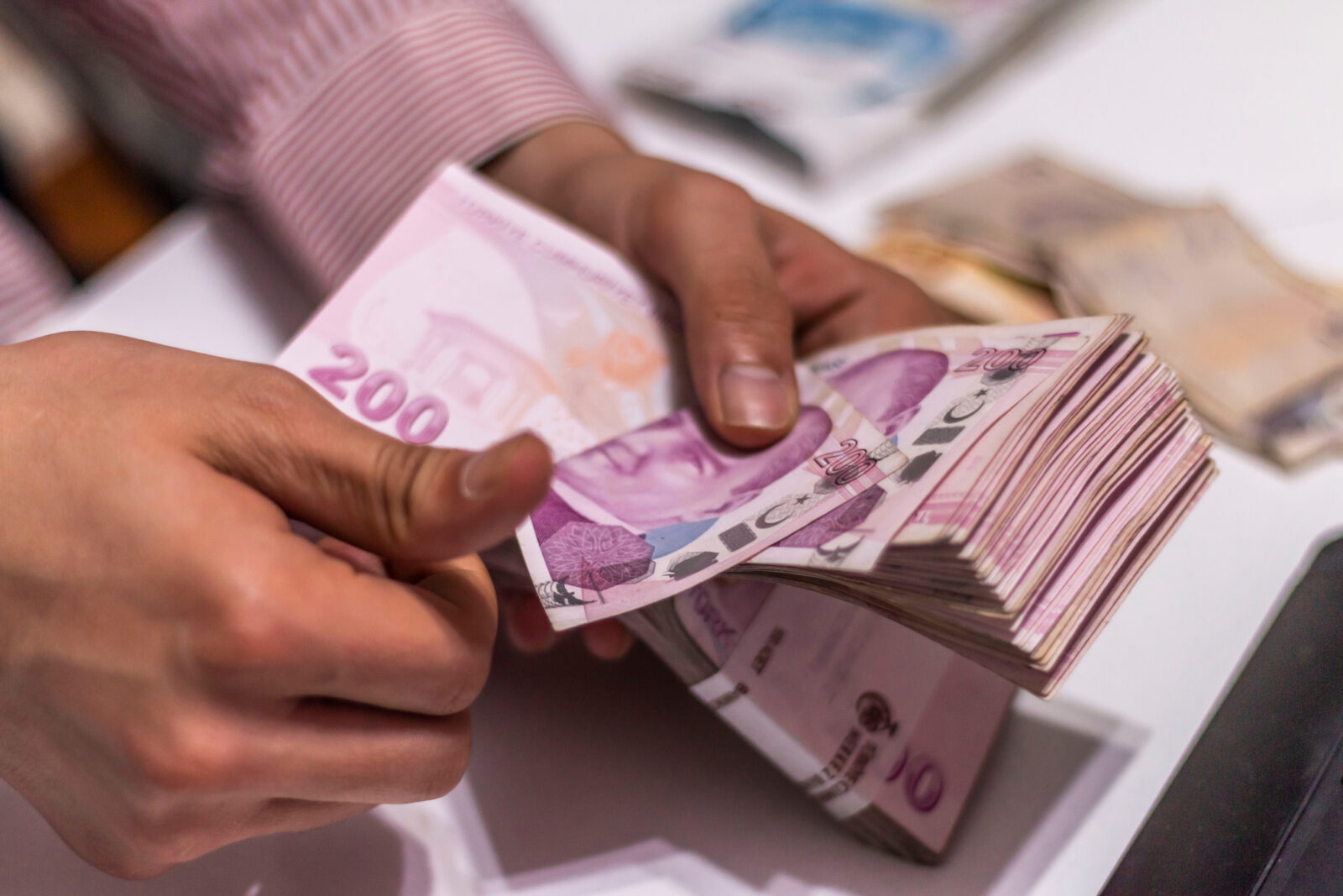 File photo shows a person counting a large stack of 200 Turkish lira banknotes at a desk, accessed on March 21, 2025. (Adobe Stock Photo)