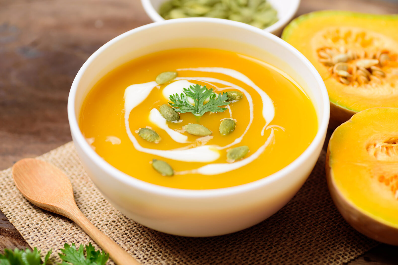 A steaming bowl of creamy pumpkin soup with a swirl of cream, garnished with pumpkin seeds and fresh herbs.
