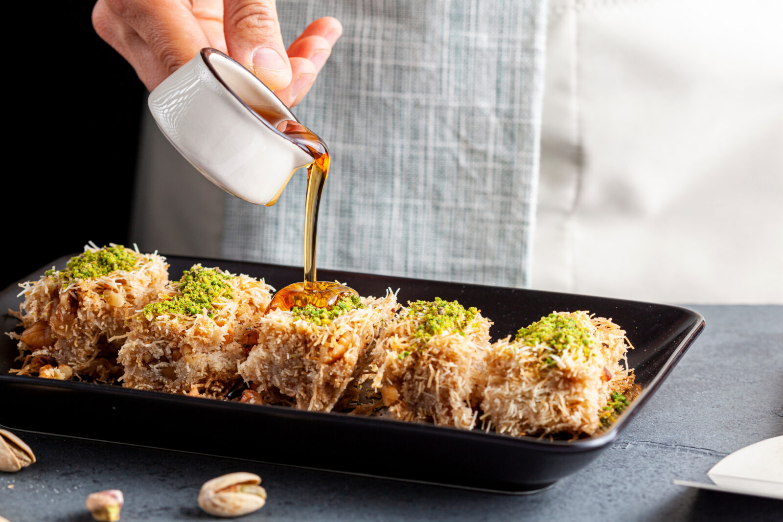 Golden brown kadaifi rolls packed with pistachios being drenched in fresh syrup, a classic dessert that adds crisp texture and nutty sweetness to any Ramadan night. (Adobe Stock Photo)