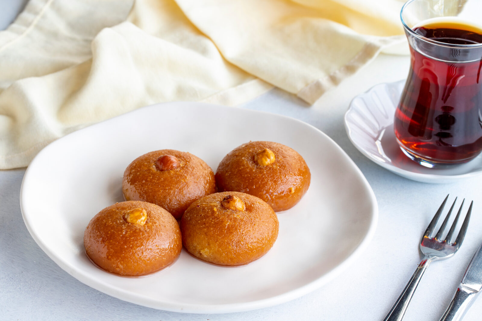 Sekerpare, soft semolina cookies soaked in syrup, served with a glass of Turkish tea for a classic dessert pairing. (Adobe Stock Photo)