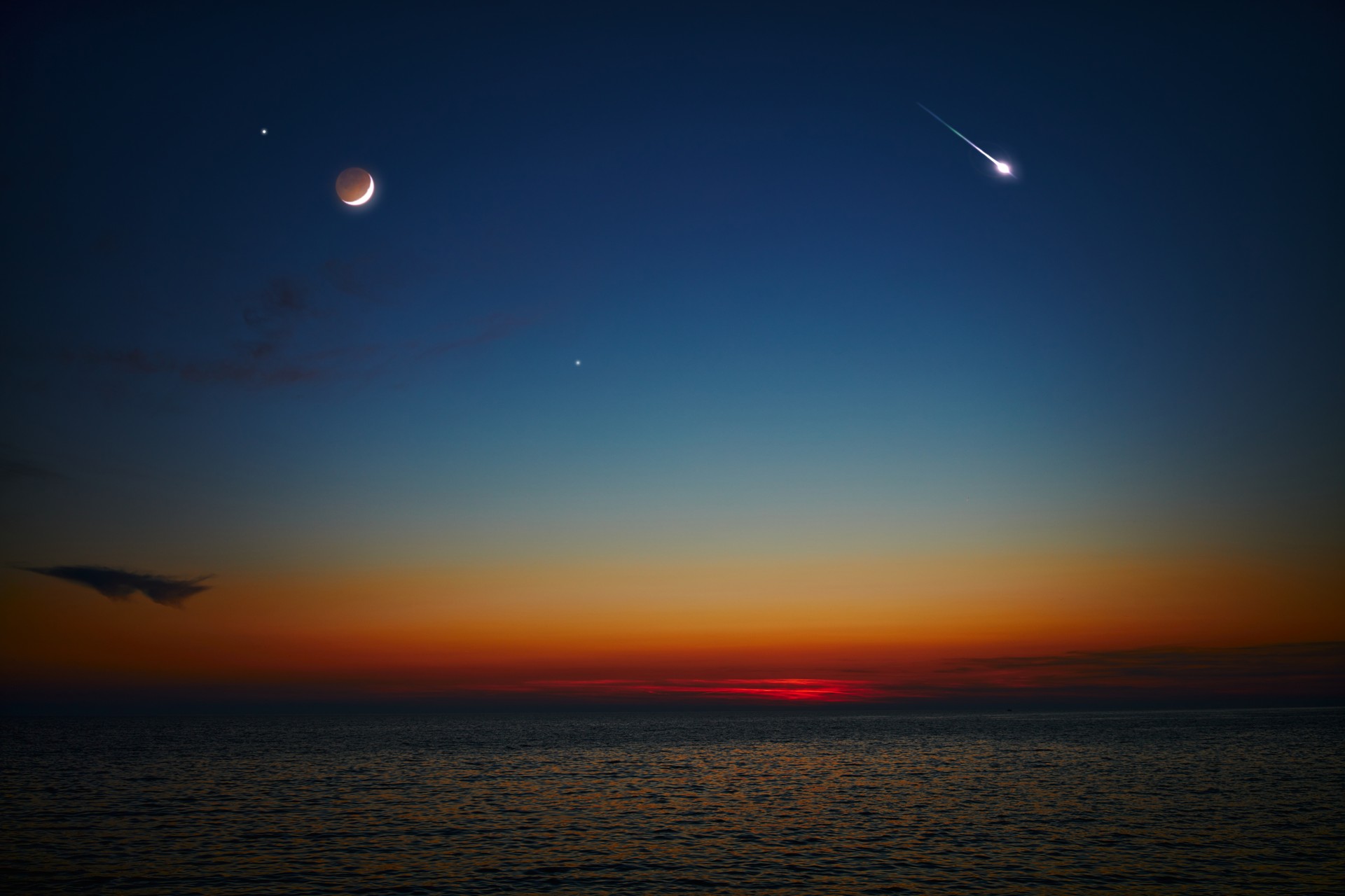 A crescent Moon, bright planets, and a meteor streak appear in the twilight sky above a calm sea, capturing a tranquil moment of celestial beauty just before sunrise. (Adobe Stock Photo)