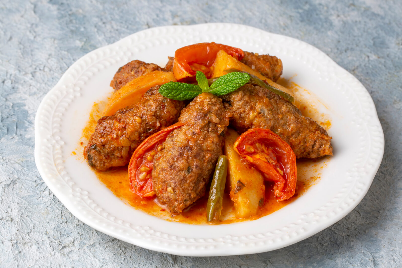 A plate of Izmir kofte with tomatoes, potatoes, and green peppers in a rich tomato sauce. (Adobe Stock Photo)