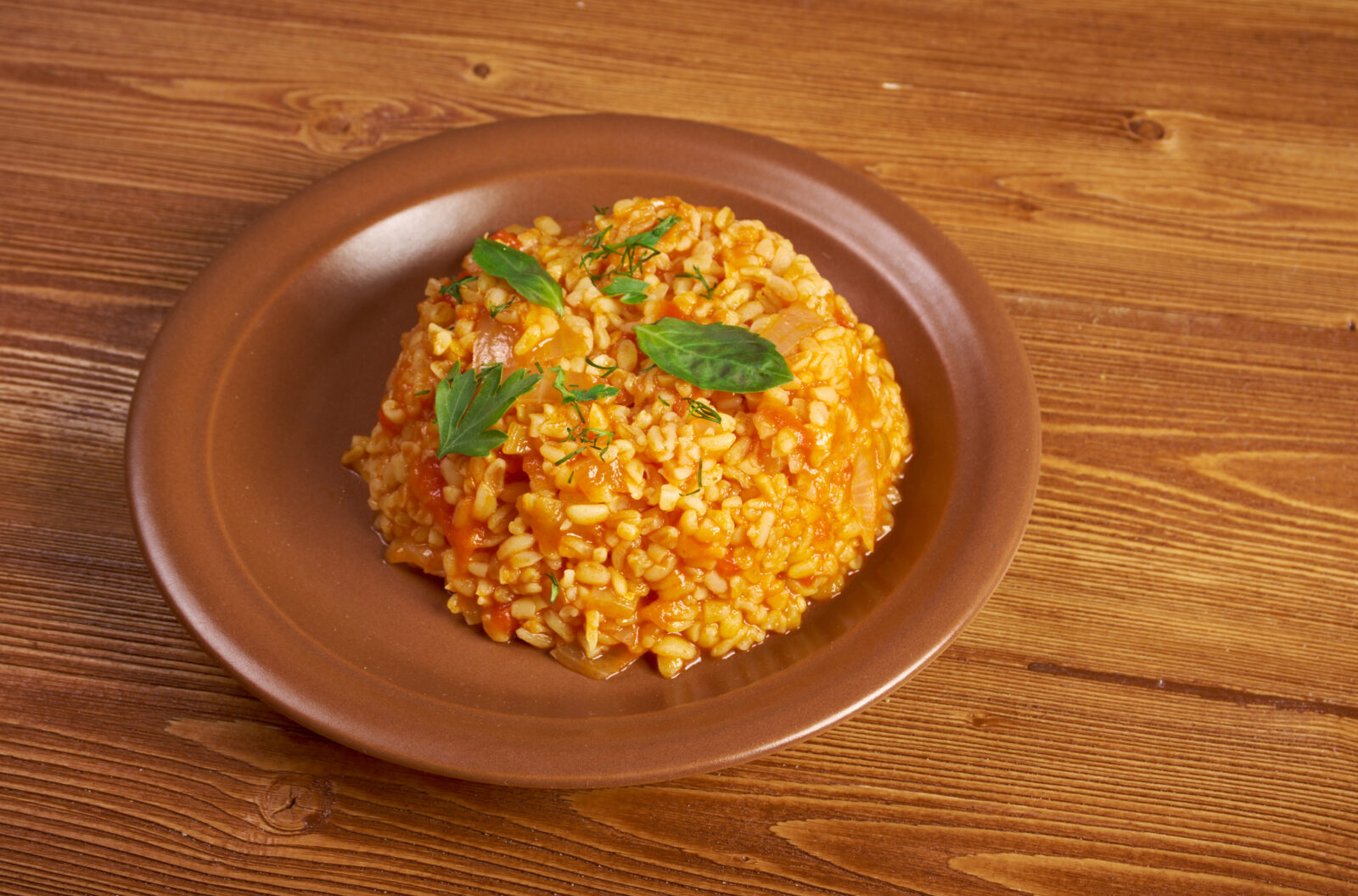 A warm and flavorful serving of Turkish-style bulgur pilaf with roasted vegetables, perfect for complementing grilled meats or hearty meals. (Adobe Stock Photo)