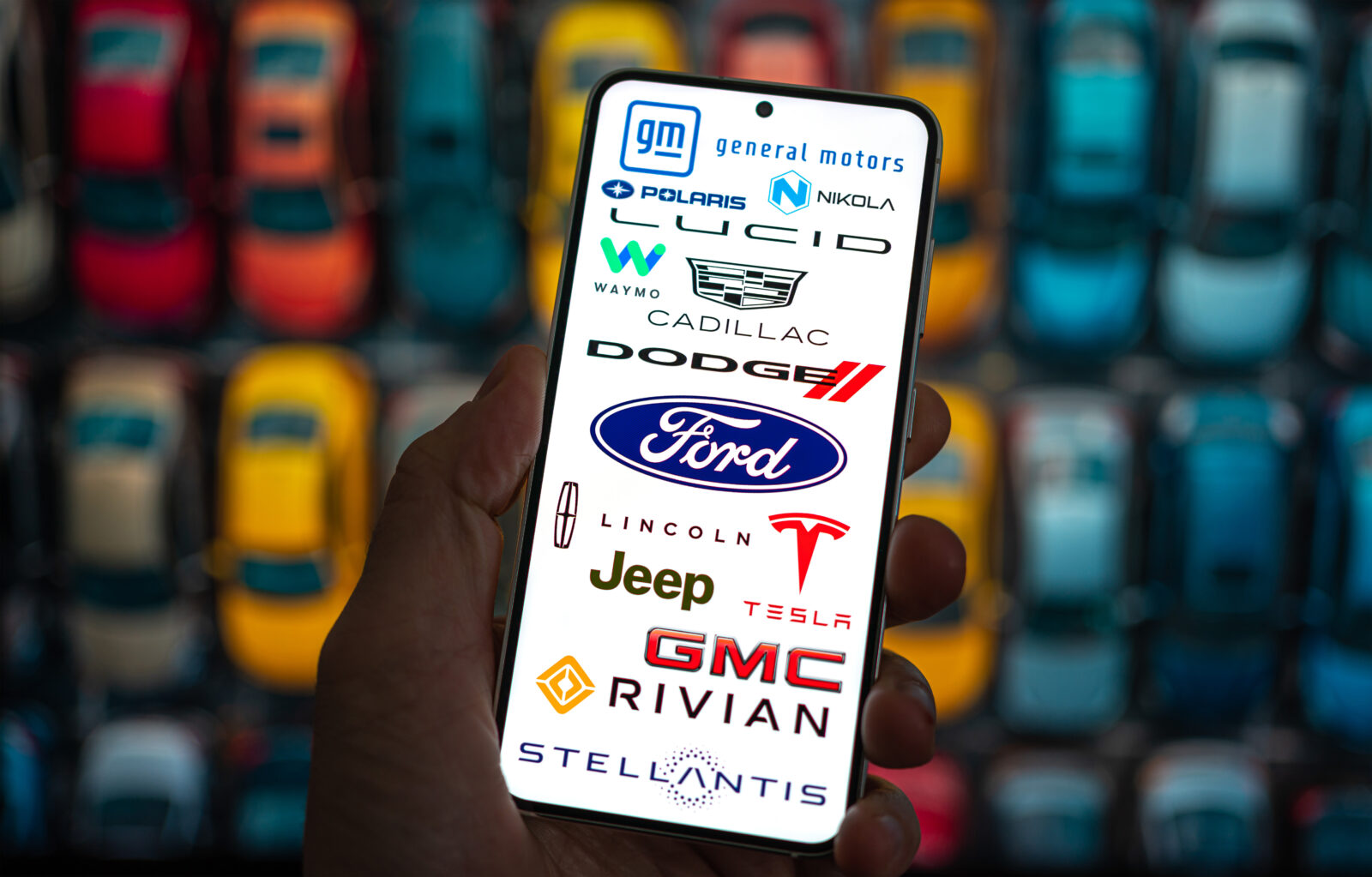 Photo illustration shows a smartphone screen displaying logos of major U.S. automakers, including General Motors, Ford, Stellantis, Tesla, and Rivian. (Adobe Stock Photo)