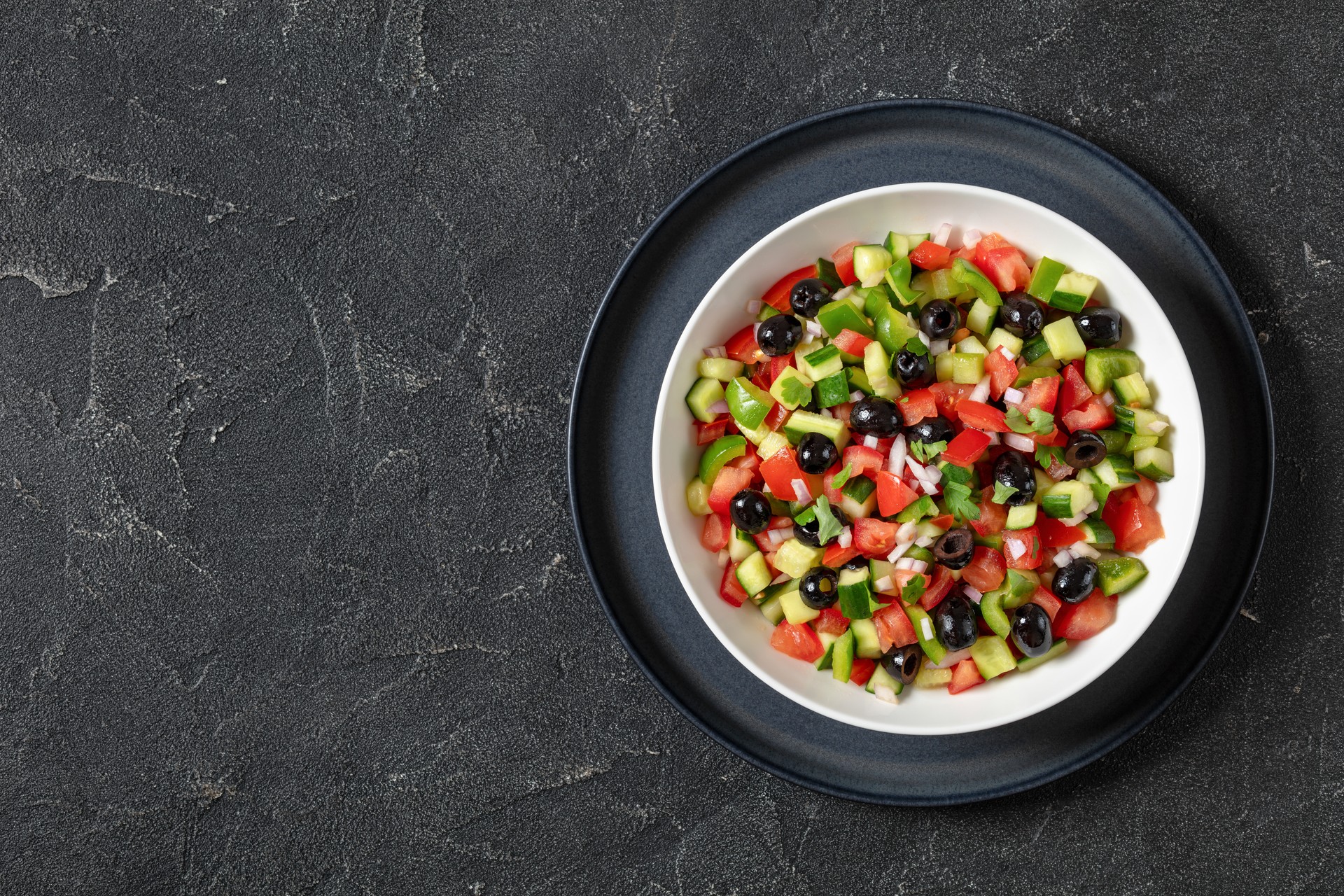 A fresh bowl of shepherd’s salad with tomatoes, cucumbers, green peppers, and black olives. (Adobe Stock Photo)