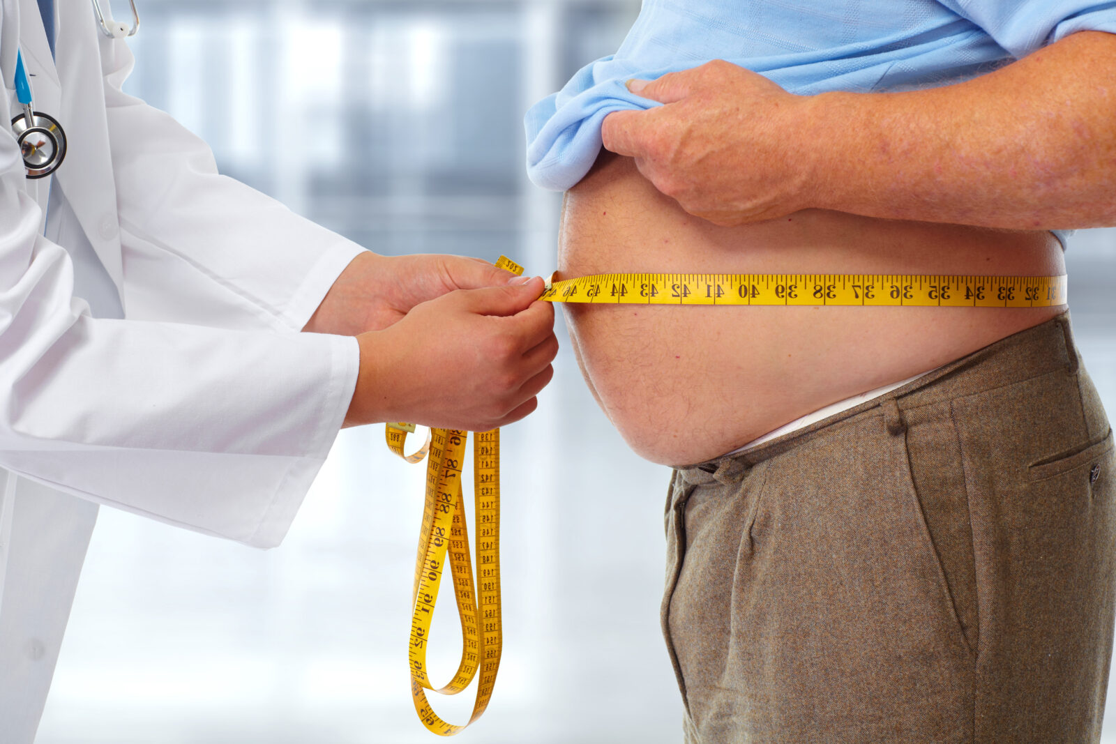 A healthcare professional measures a patient's waistline to assess obesity-related health risks. (Adobe Stock Photo)