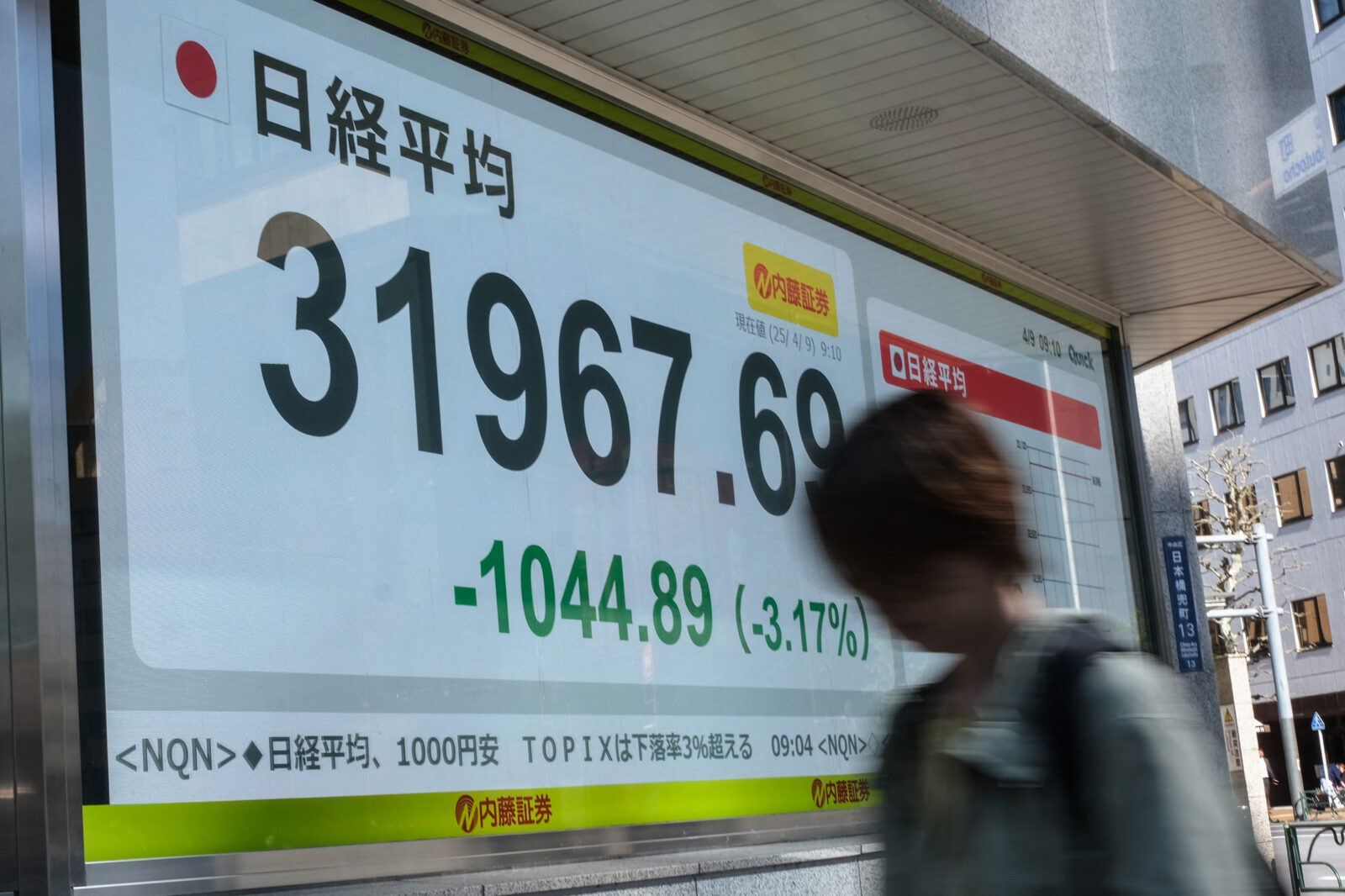 A woman walks past an electronic board showing the numbers of the Nikkei Stock Average on the Tokyo Stock Exchange in Tokyo on April 9, 2025. (AFP Photo)
