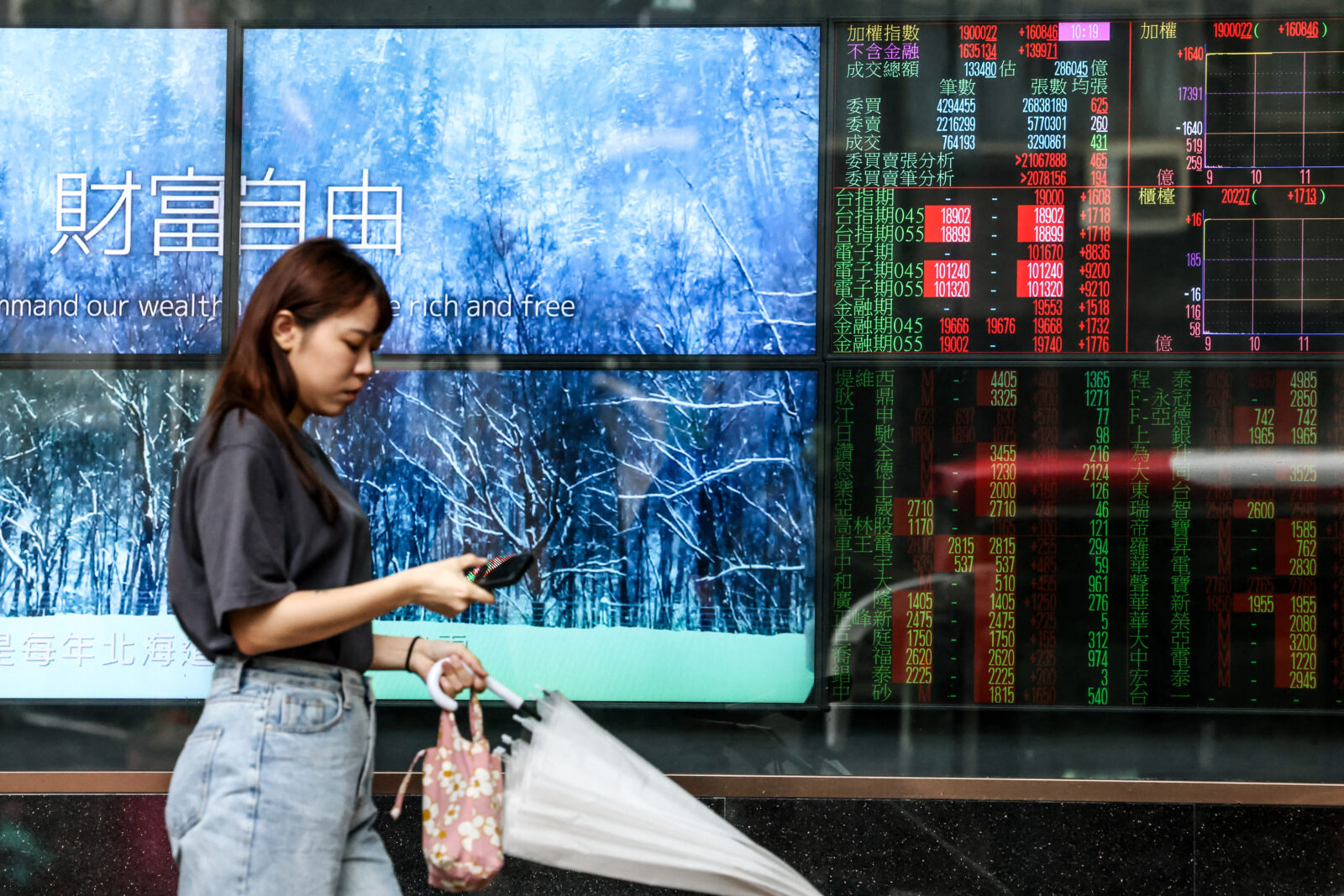 A woman walks past a screen showing share prices of the Taiwan stock market in Taipei on April 10, 2025. (AFP Photo)