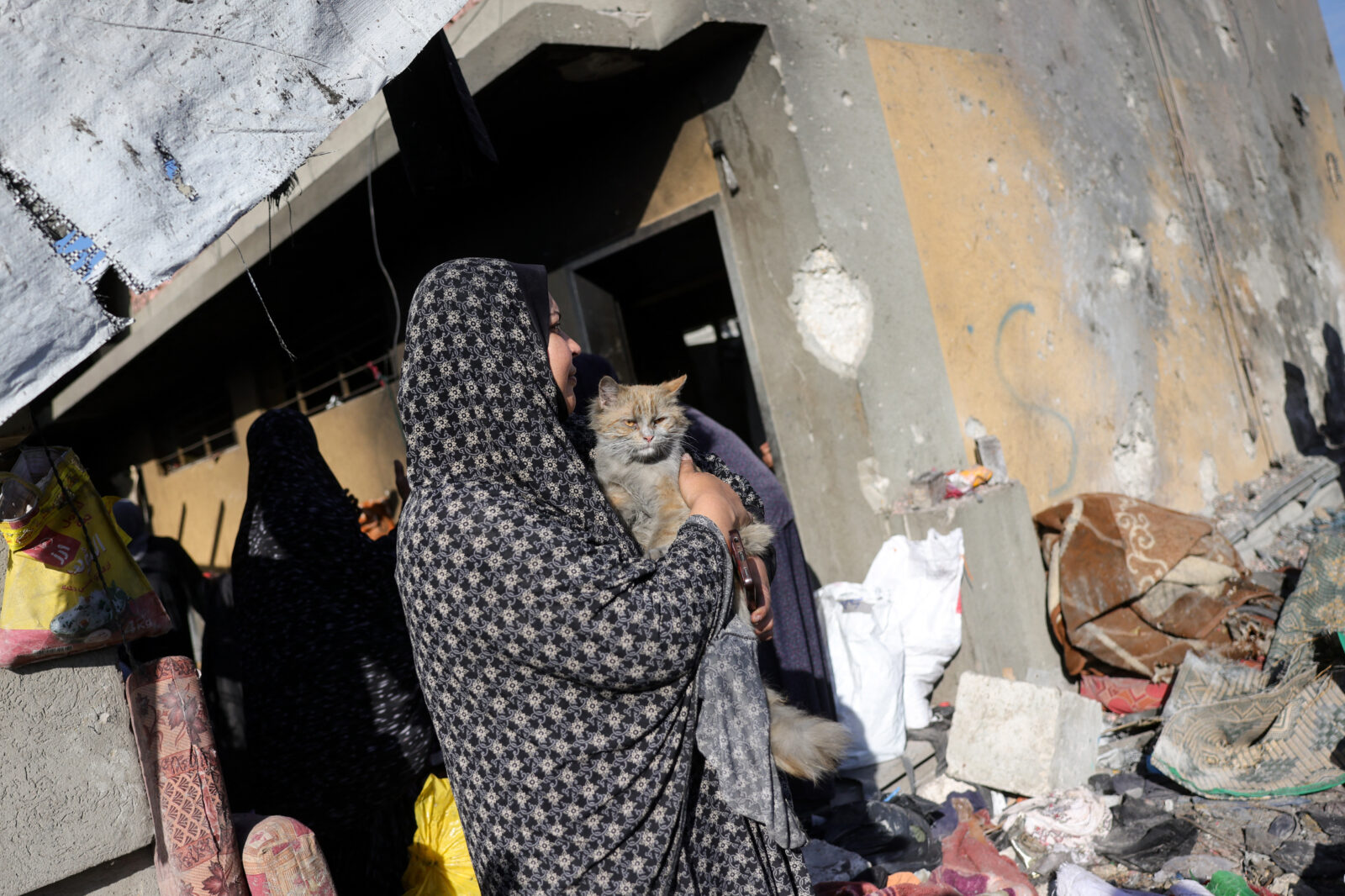 A Palestinian woman holding a cat stands amid the destruction following an Israeli strike that hit a school-turned-shelter in Gaza City on April 13, 2025. (AFP Photo)