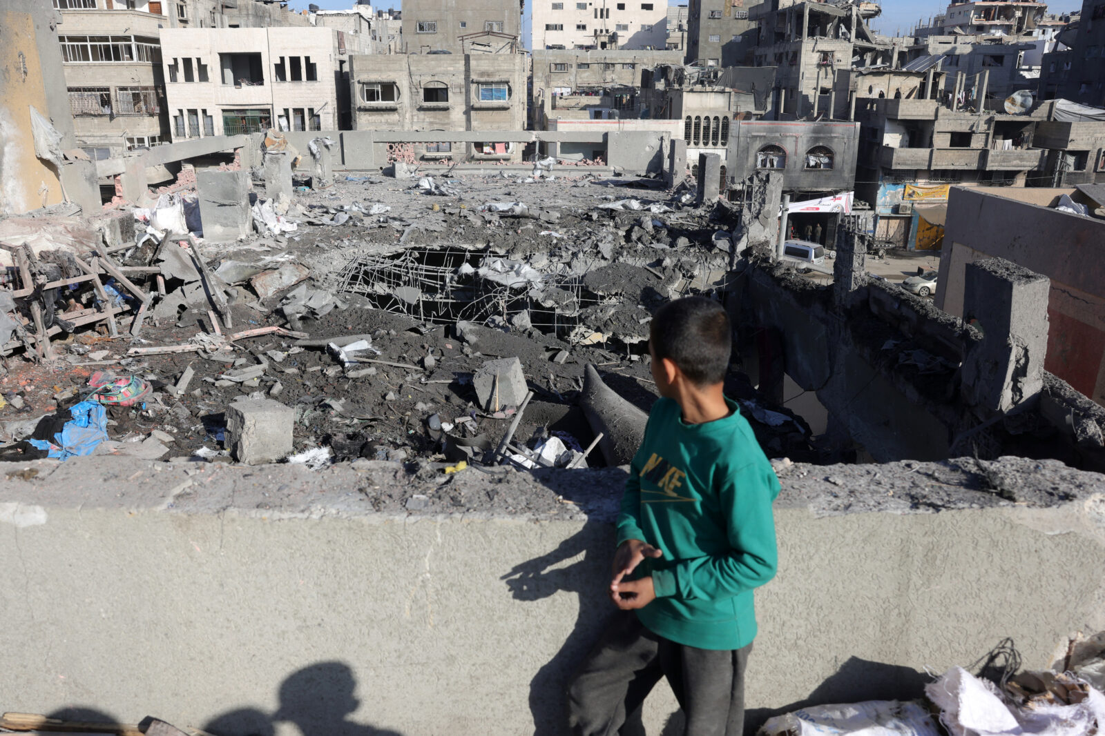 A Palestinian child standing on a rooftop stares at the destruction