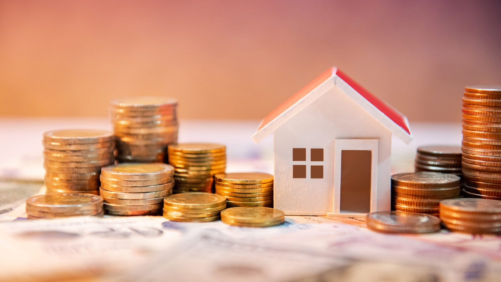 Real estate investment concept—rising housing costs and financial planning represented by a miniature house surrounded by stacks of coins, accessed on April 4, 2025. (Adobe Stock Photo)