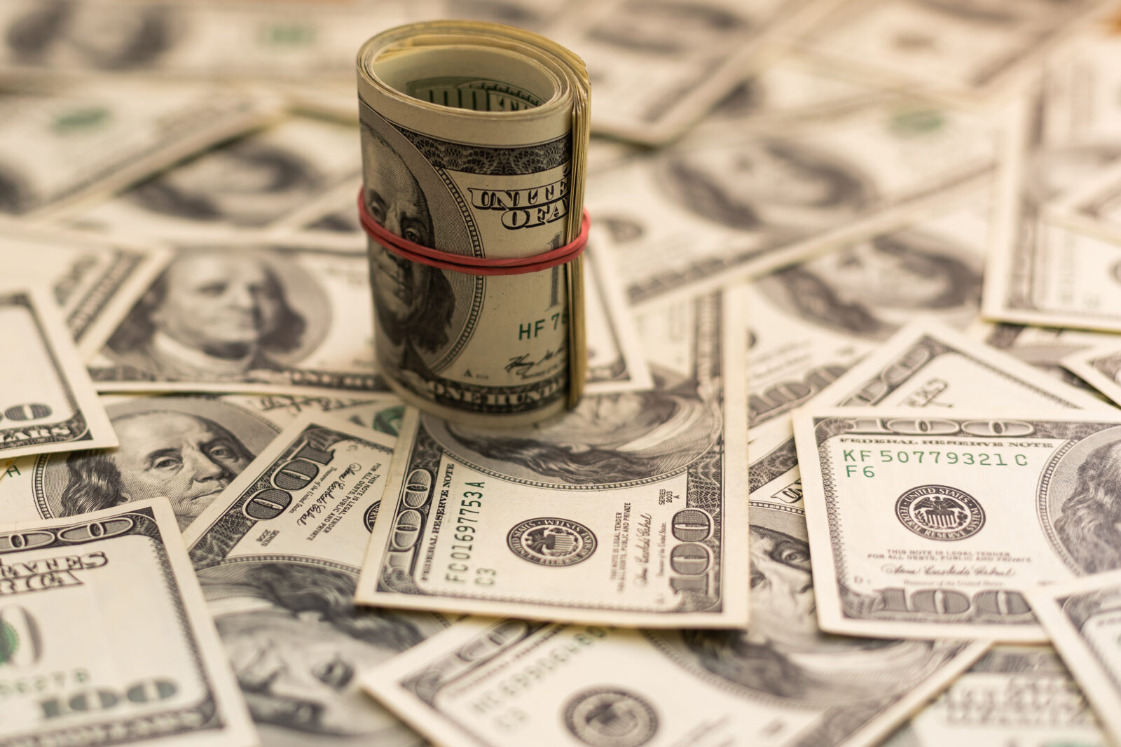 Photo illustration shows a tightly rolled bundle of U.S. $100 bills sitting on a scattered pile of banknotes, accessed on April 2, 2025. (Adobe Stock Photo)