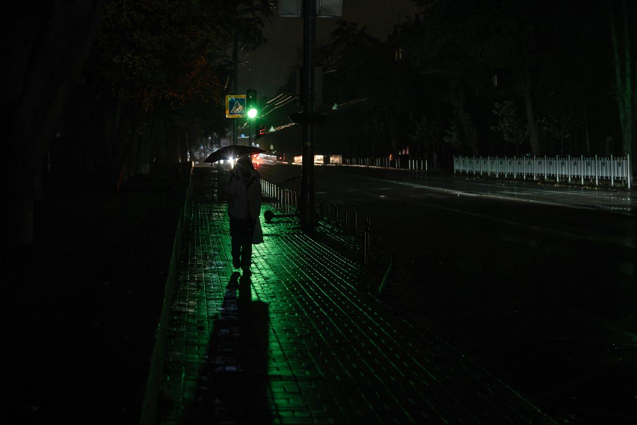 A woman with an umbrella walks down a street during a power outage in Kyiv on October 10, 2025. (AFP Photo)
