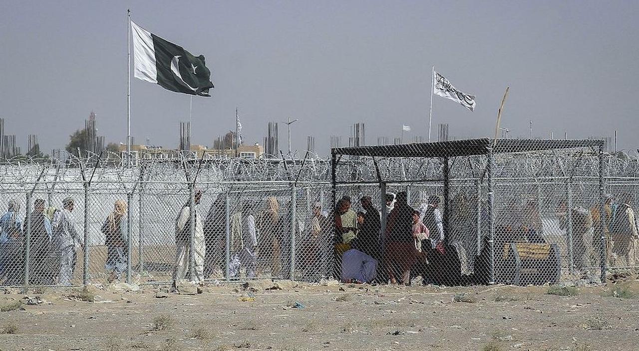 Afghan and Pakistani nationals walk through a security barrier to cross the border as a national flag of Pakistan and a Taliban flag is masted in the Pakistan-Afghanistan border crossing point in Chaman, Aug. 24, 2021. (AFP Photo)