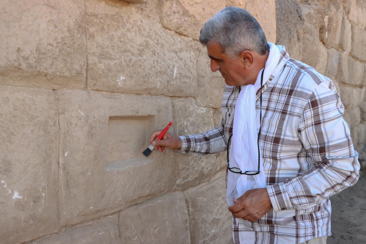 Professor Rafet Cavusoglu, head of the excavation team, carefully cleans one of the newly uncovered inscriptions on the fortification wall at Zernaki Hill in Van’s Ercis district, eastern Türkiye, Oct. 8, 2025. (AA Photo)