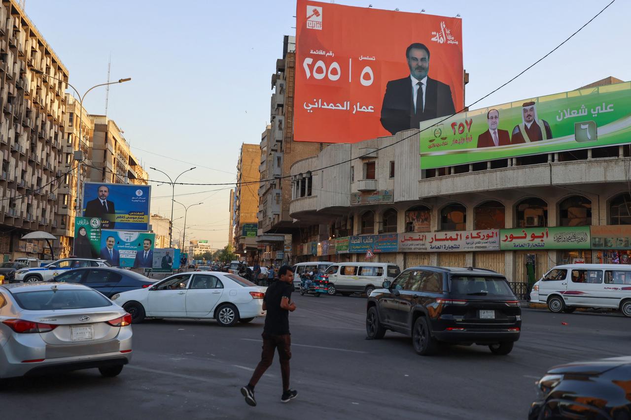 People drive their vehicles past electoral billboards  on a street in Baghdad on October 14, 2025 . (AFP Photo )