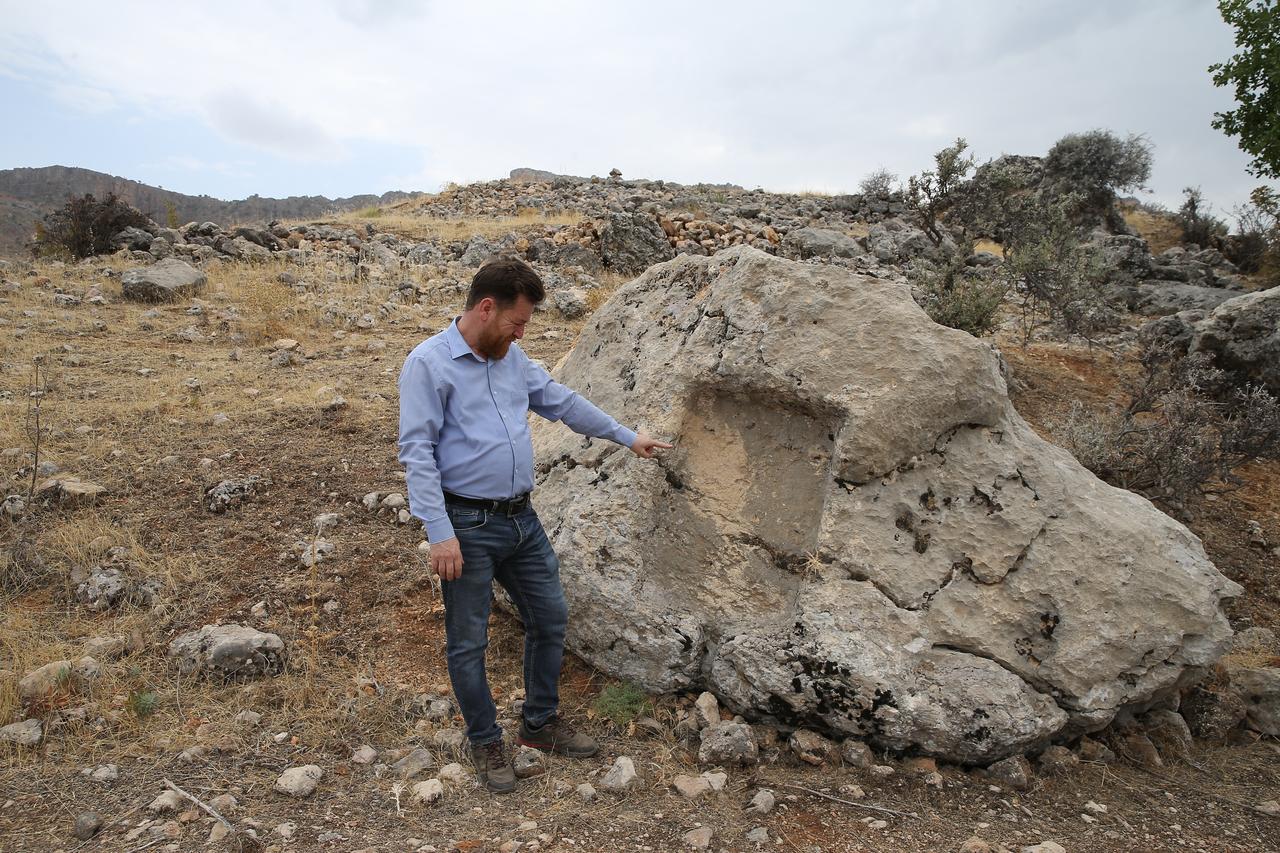 Adiyaman Museum Director Mehmet Alkan examines a rock-cut feature believed to have been used in wine production at the newly identified Roman-era settlement in Gerger district, southeastern Türkiye, Oct. 16, 2025. (AA Photo)