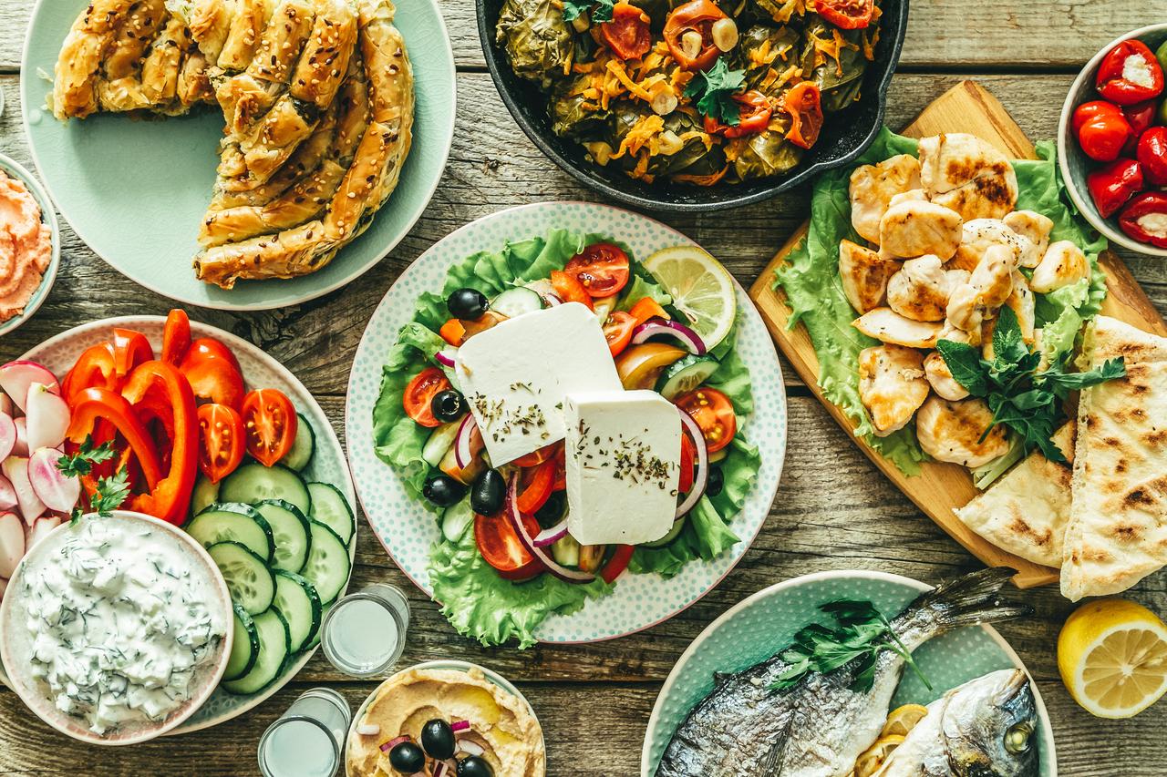 A variety of traditional Mediterranean dishes, including Greek salad, stuffed vine leaves, grilled fish, and feta cheese, served on a rustic wooden table. (Photo via Adobe Stock)