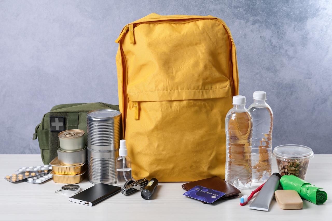 Emergency survival kit with various essential supplies arranged on a white wooden table. (Adobe Stock Photo)