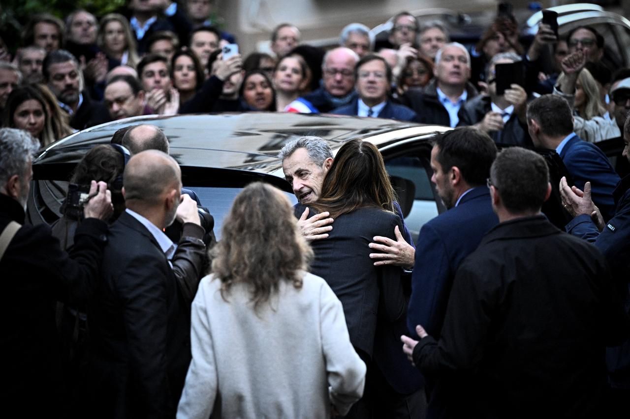 Frances former president Nicolas Sarkozy (C) hugs his wife Carla Bruni-Sarkozy as he leaves his residence to present himself to La Sante Prison for incarceration on a five-year prison sentence after being convicted of criminal conspiracy over a plan for late Libyan dictator Moamer Kadhafi to fund his 2007 electoral campaign, in Paris, on October 21, 2025. (AFP Photo)