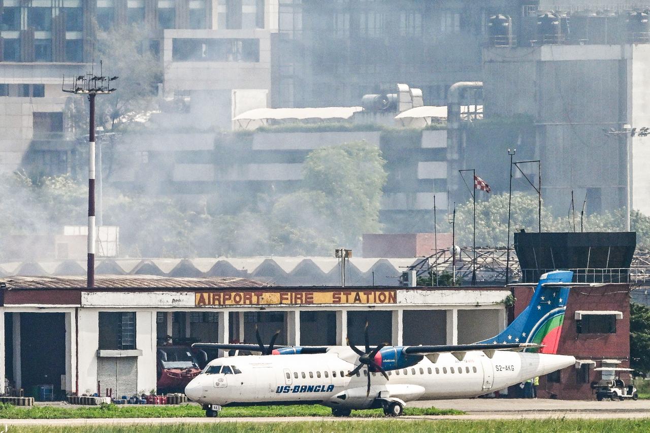 An aircraft prepares to take off as smoke rises from the fire-damaged cargo terminal of Hazrat Shahjalal International Airport, a day after the blaze in Dhaka on Oct. 19, 2025. (AFP Photo)
