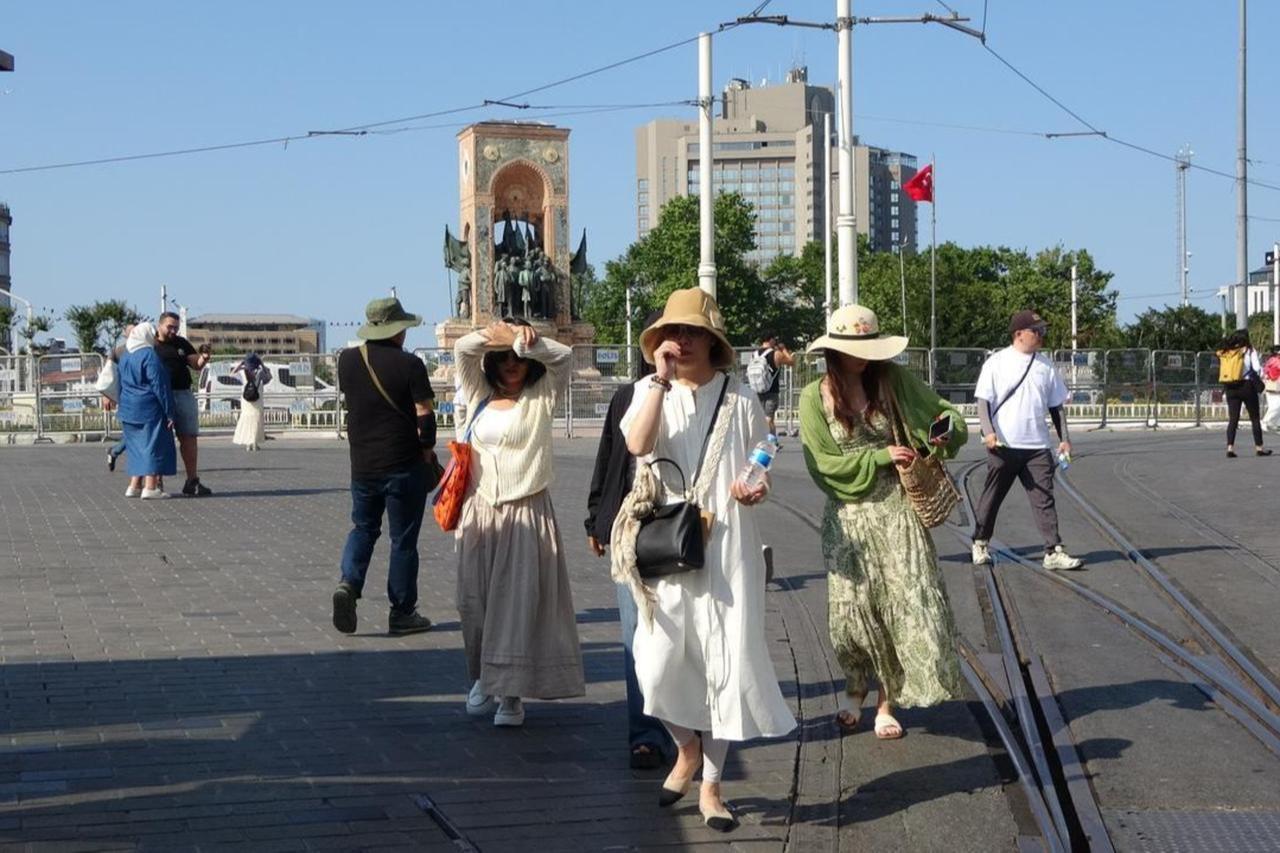 Tourists seek shade from the sun as they walk through Taksim Square, Istanbul, Türkiye, June 18, 2025. (IHA Photo)