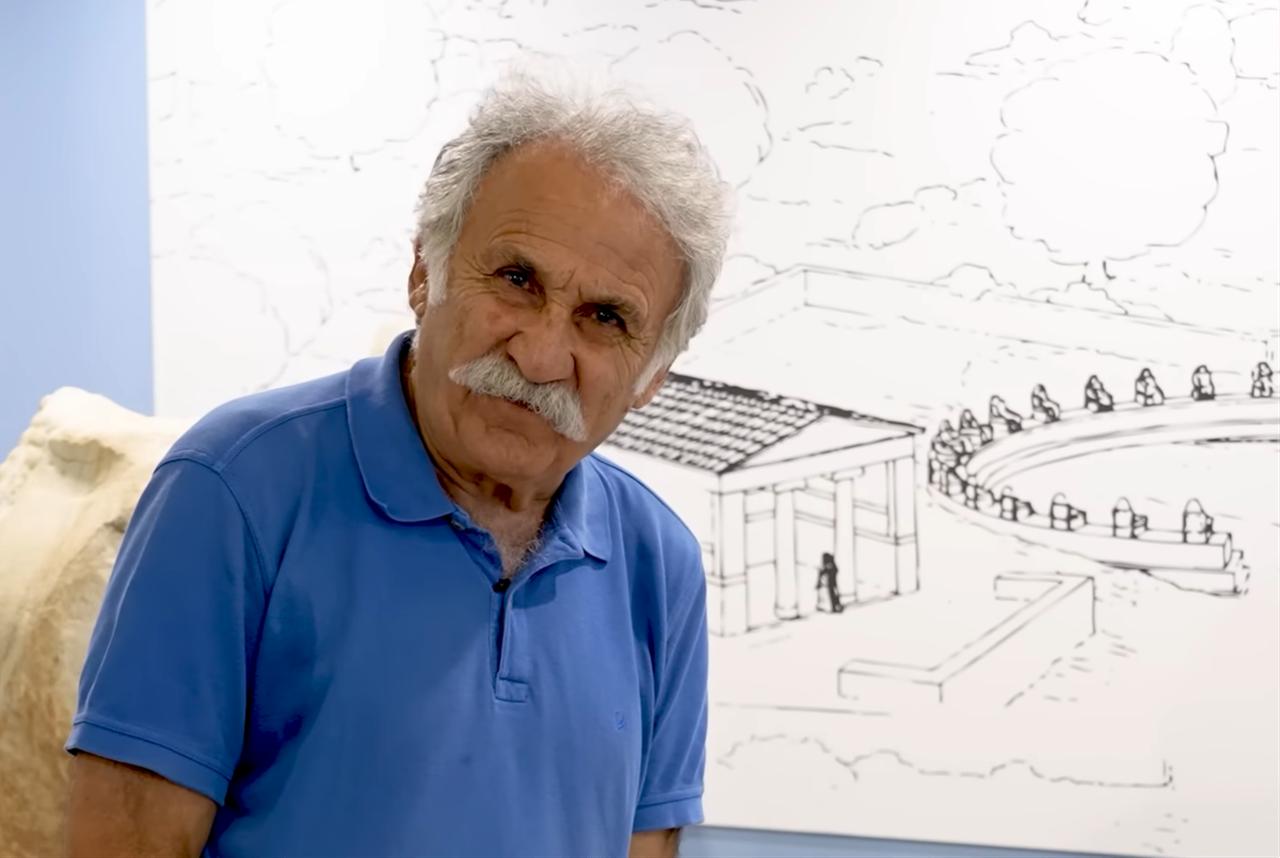 Professor Fahri Isik standing beside an illustration of ancient structures, discussing the city’s architectural heritage. (Photo via YouTube/@issanat)
